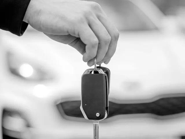 Hand holding a flip key with the blade folded out in front of a parked car