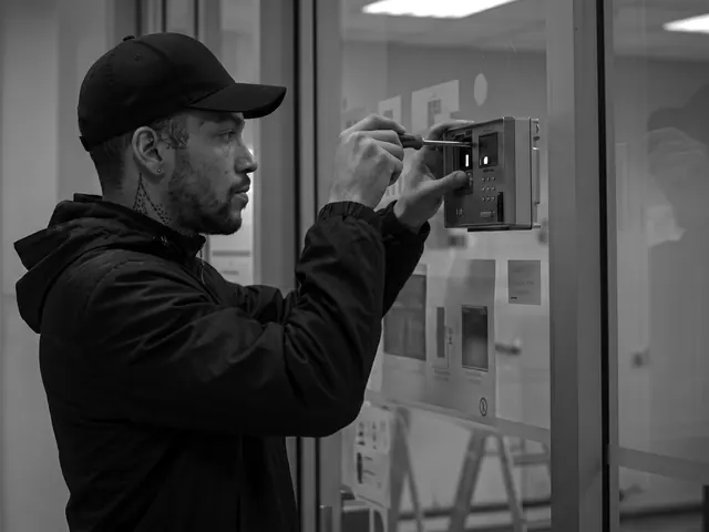 Locksmith in a black cap fitting an access control keypad reader beside a glass office door