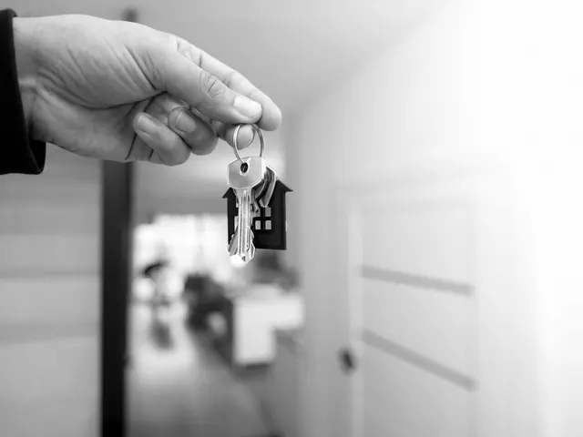 Hand holding a set of new house keys on a ring with a house-shaped tag inside a hallway