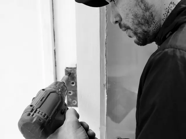 Locksmith with a cordless drill fitting a strike plate on a white door frame